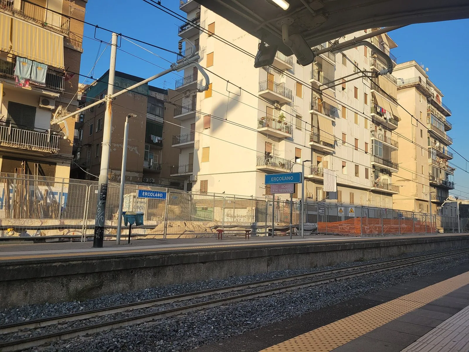 Banchina della stazione Circumvesuviana di Ercolano con i cartelli Ercolano e Scavi Vesuvio e i palazzi del quartiere alle spalle