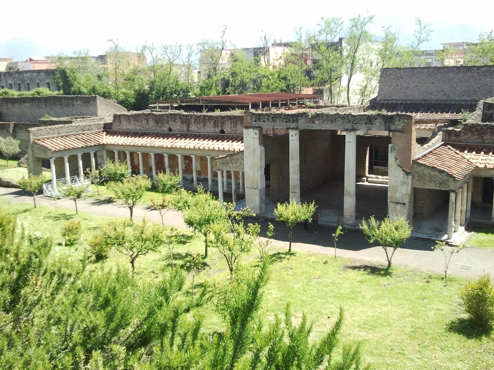 Portici con colonne e tetti in coppi della Villa di Poppea a Oplontis, circondati da prati e giovani alberi