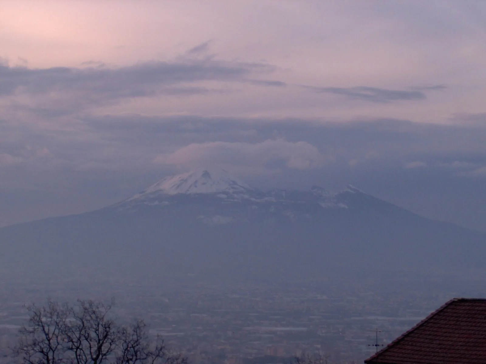 Il Vesuvio con la cima coperta di neve sotto un cielo nuvoloso al crepuscolo, con la pianura vesuviana avvolta nella foschia